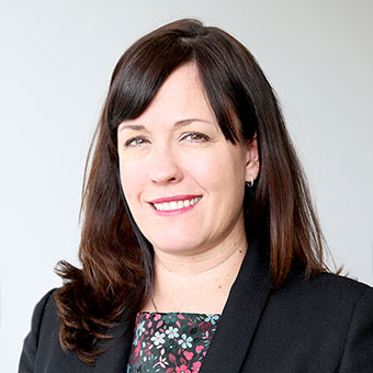 Person smiling, wearing a dark blazer, neutral background.