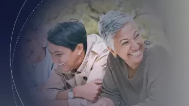 Three people sitting together, smiling and laughing outdoors.