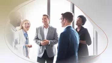 Group of people in professional attire having a discussion by large windows.