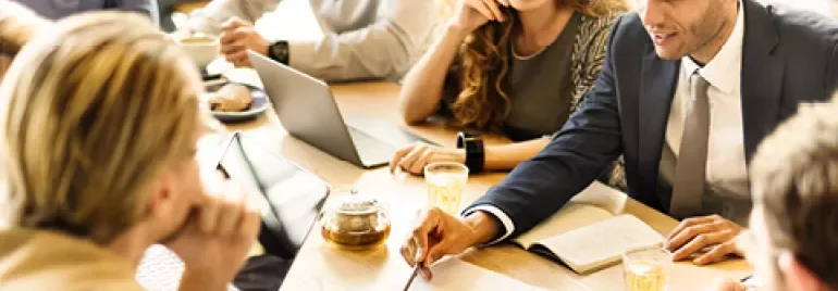 Group of people discussing in a meeting with laptops and notebooks on a table.